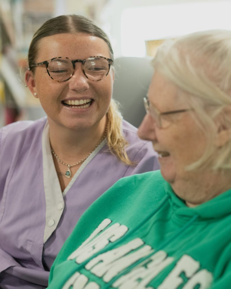 A carer and an older woman laughing together indoors