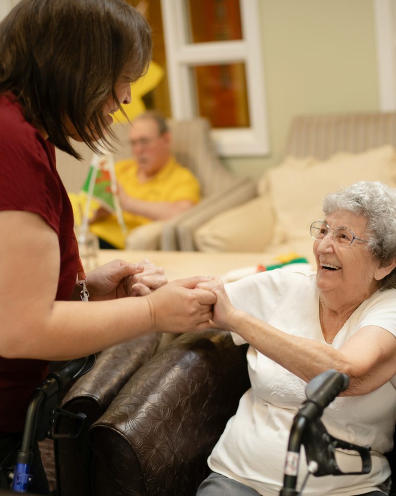 A care worker in scrubs leaning in to talk with an older person