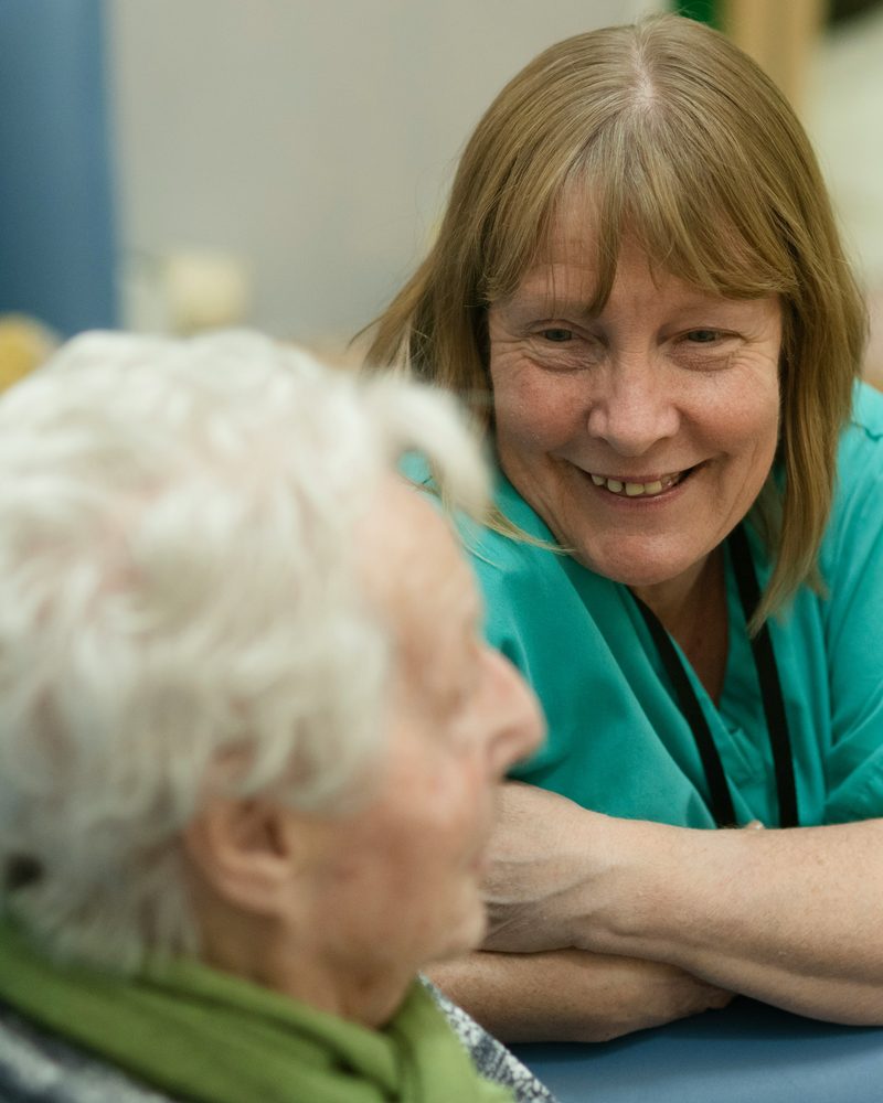 A carer supporting an older woman who is using a walking frame