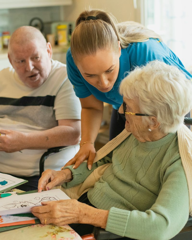 A carer helping an older couple with a colouring activity