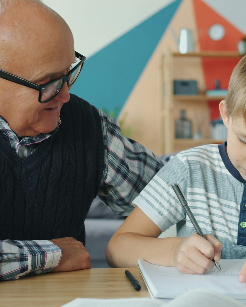 A grandfather helping his grandson with homework at a table