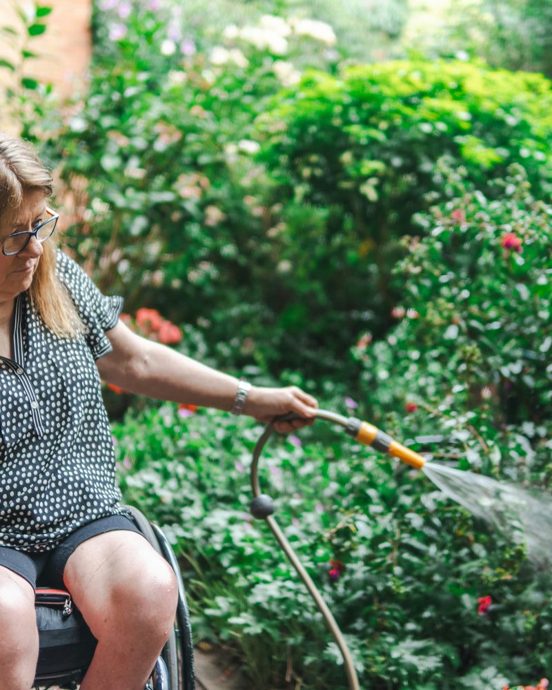 A woman in a wheelchair watering plants in a garden