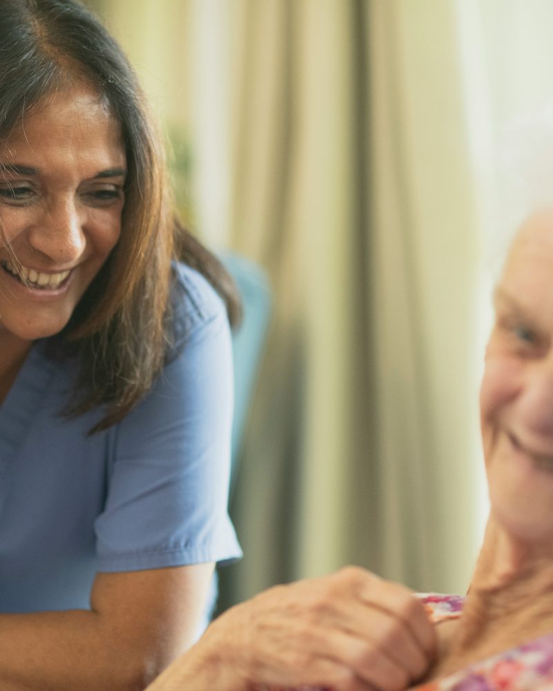 A nurse smiling with an older person in their room